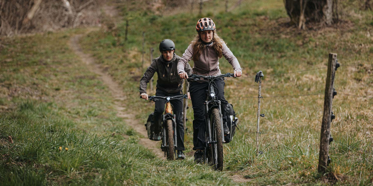 Pärchen mit Trekking E-Bikes nimmt schmalen Pfad querfeldein