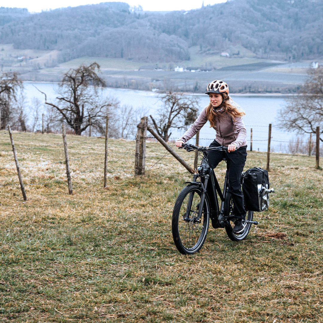 Fahrradfahrerin auf Trekking-Tour fährt Wiesenhügel bergauf