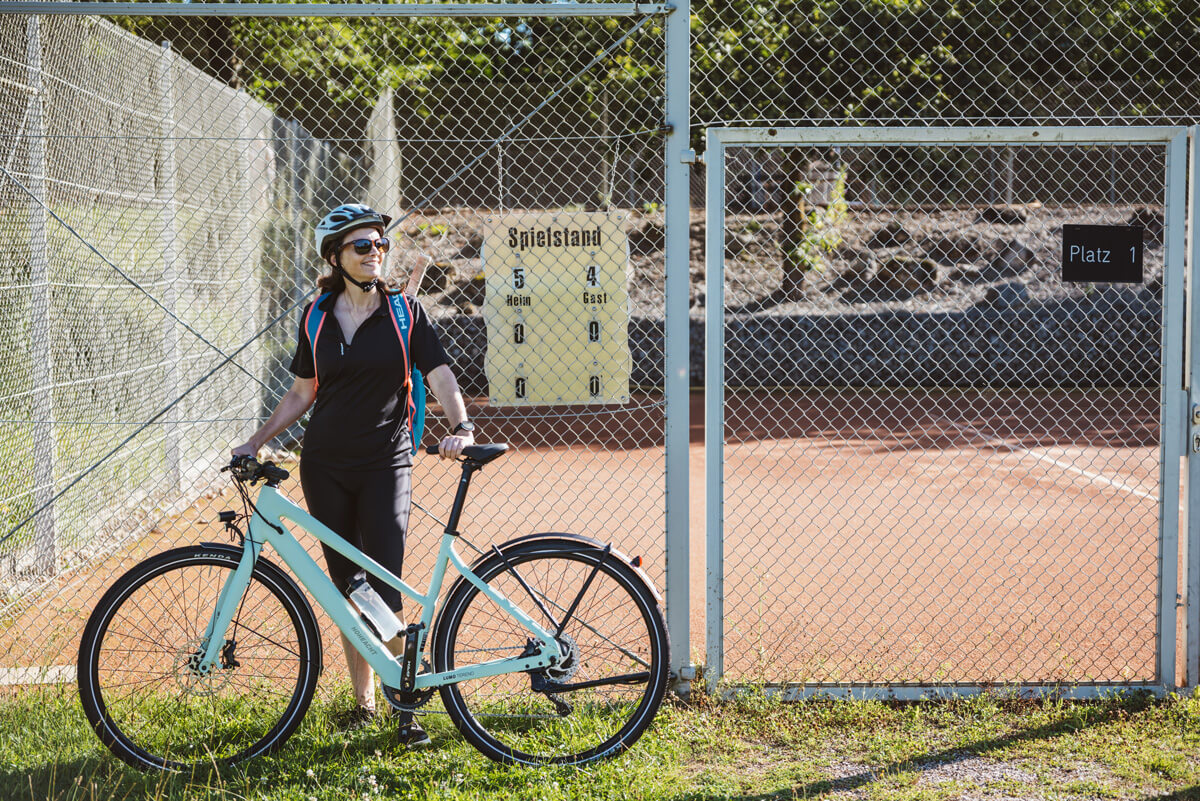 Fahrradfahrerin mit ihrem LUMO Tereno vor einem Tennisplatz